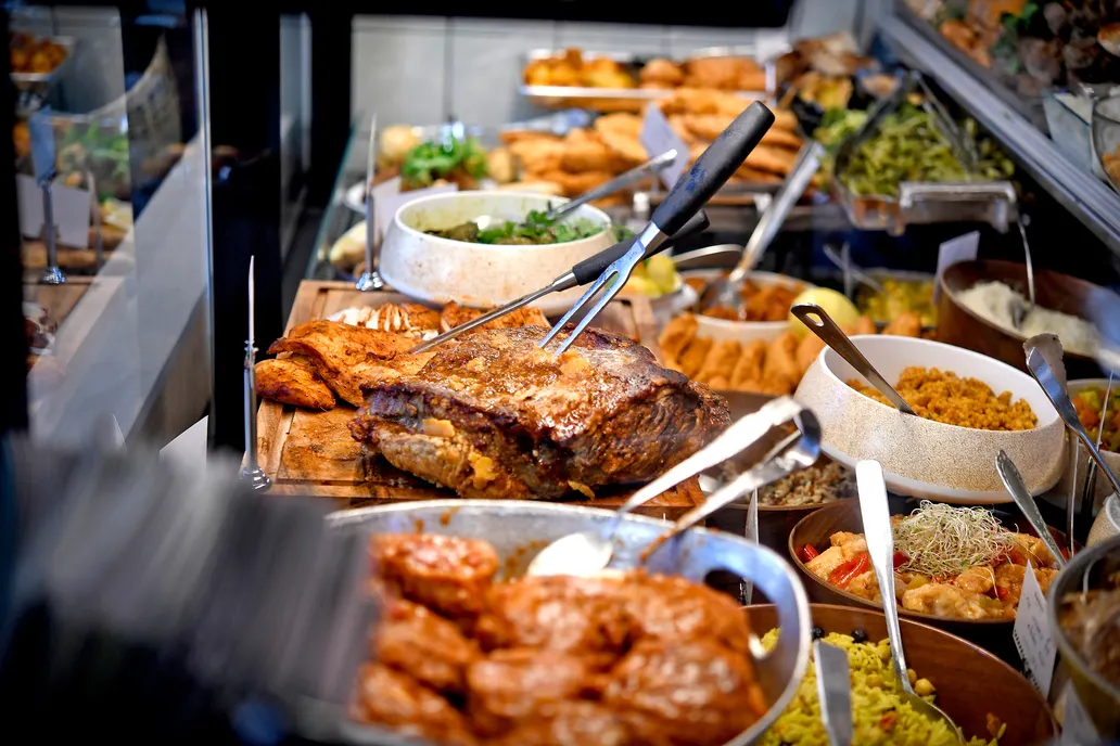 תקריב על נתחי בשר צלויים, תוספות ומטוגנים בתוך הויטרינה של מעדניית דאדי.