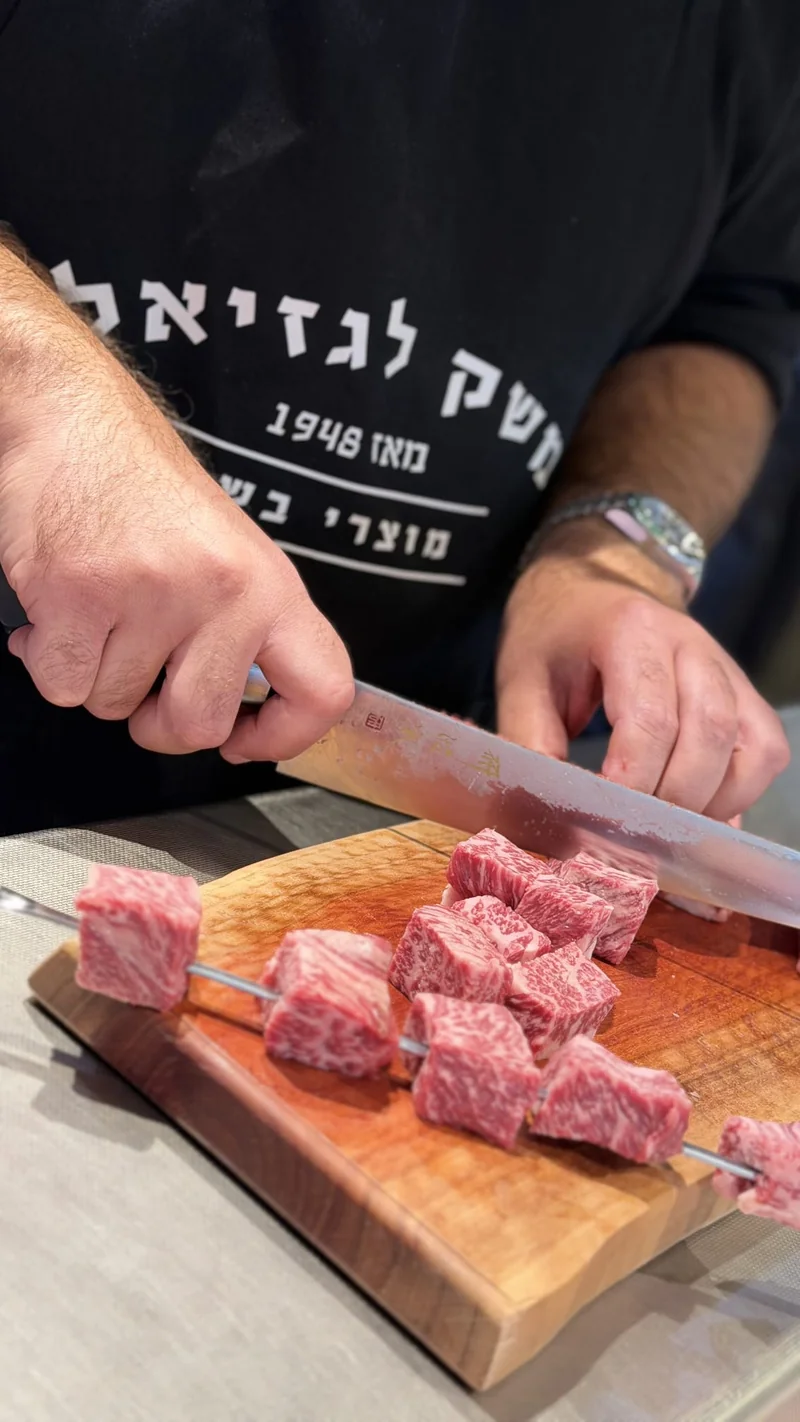 ידיים חותכות קוביות בשר אדומות ועסיסיות על קרש עץ