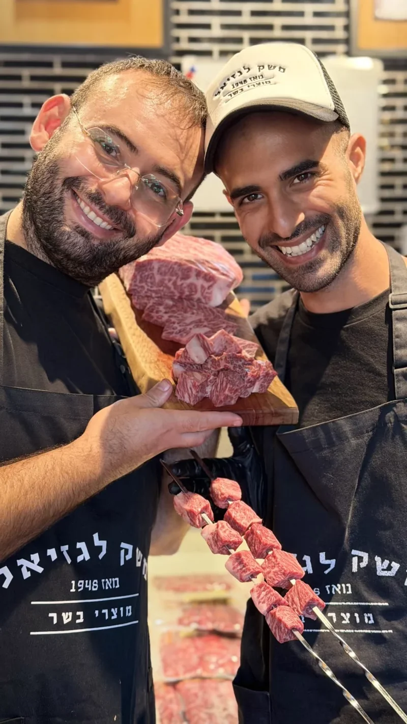 שני גברים מחייכים מחזיקים שיפודי בקר אדום טריים בפסטיבל.