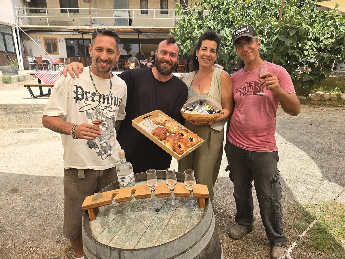 ארבעה אנשים מחייכים, אחד מחזיק מגש מאפים ואחד בקבוק ג'ין.